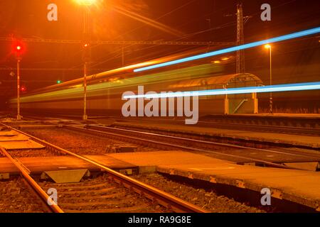 Bianco e blu treno passa una piccola scoperchiata stazione ferroviaria di notte nella Repubblica Ceca. Sfocata treno di movimento Foto Stock