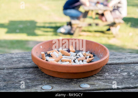 Posacenere in terracotta con un sacco di mozziconi di sigarette o mozziconi di sigaretta su un tavolo esterno, England, Regno Unito Foto Stock