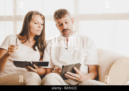 Il marito e la moglie su un lettino nel loro appartamento con una tavoletta e di un blocco note Foto Stock