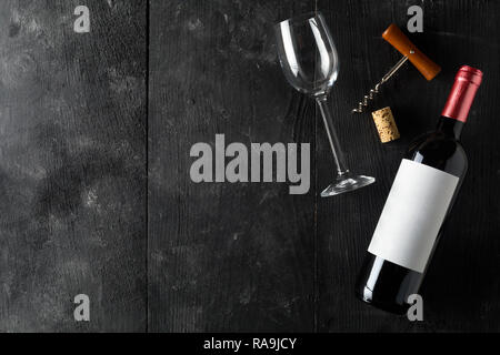 Rosso bottiglia di vino con cavatappi, sughero e vino in vetro scuro sul tavolo di legno piana da laici al di sopra con lo spazio di copia Foto Stock