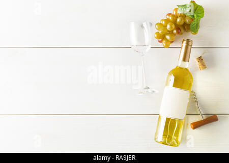 Bianco bottiglia di vino con uve, cavatappi, sughero e bicchiere di vino bianco sul tavolo di legno piana da laici al di sopra con lo spazio di copia Foto Stock