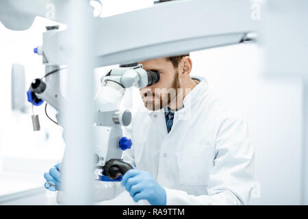 Dentista maschio esame paziente cercando sui denti con microscopio professionale presso la Chirurgia studio dentistico Foto Stock