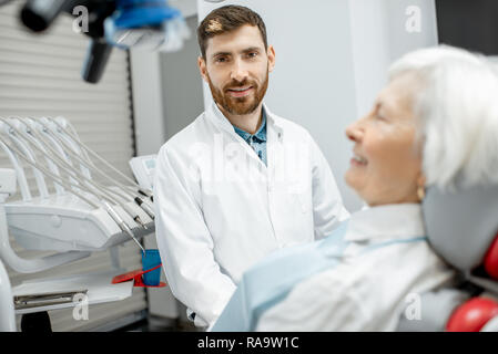 Bello il dentista durante la consultazione con il senior donna nello studio dentistico Foto Stock