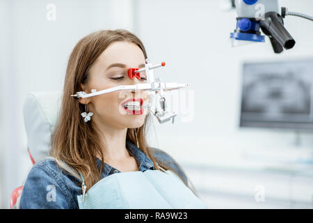 Giovane donna paziente ganascia con sistema di misurazione sul suo viso seduto in studio dentistico Foto Stock