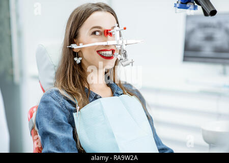 Giovane donna paziente ganascia con sistema di misurazione sul suo viso seduto in studio dentistico Foto Stock