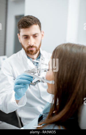 Dentista ganascia mettendo il sistema di misura a una giovane donna paziente nello studio dentistico Foto Stock