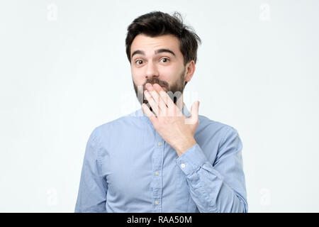 Ood cercando ispanico Giovane Uomo in camicia blu che copre la bocca con la mano Foto Stock