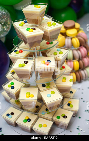 Mousse in bicchieri e colorati macarons francese torta multilivello piramide sul dessert in plastica stand. colorati macarons francesi disposti sulla piramide Foto Stock