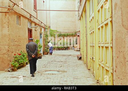 La Street View di un vecchio uigura musulmana uomo a camminare per la strada nel piccolo vicolo di edifici ristrutturati zona in Kashgar Old Town, Xinjiang, Cina. Foto Stock