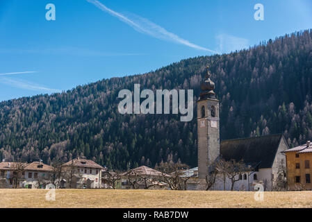 Vecchia chiesa cattolica italiana con torre campanaria, circondato da case, alberi e collina. Pellizzano - Comune città di Trento, Trentino, Italia Foto Stock