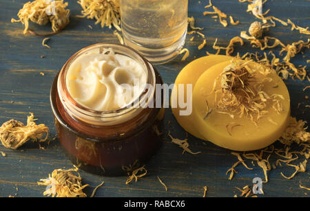 Crema per il viso di calendula e cera d'api, su un blu sullo sfondo di legno Foto Stock