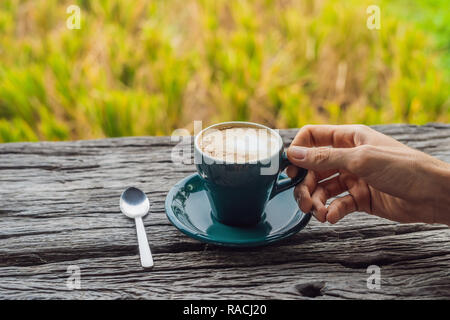 Una mano d'uomo detiene una tazza di caffè sullo sfondo di un vecchio tavolo in legno banner, formato lungo Foto Stock