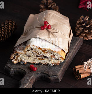 Europea tradizionale Stollen con torta di noci e frutta candita avvolto in un marrone pezzo di carta su una tavola di legno Foto Stock