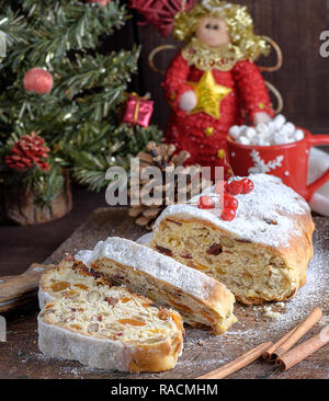 Lo Stollen, un tradizionale europea con torta di noci e frutta candita, è spolverato con zucchero a velo e tagliare a pezzi su un marrone di legno Foto Stock