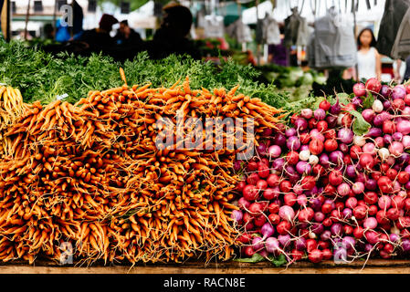 Orange baby carote e ravanelli impilati sul tavolo nel mercato locale Foto Stock