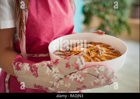 Ragazza in un grembiule rosa detiene una fetta di torta di mele. Torte fatte in casa in forma di ceramica Foto Stock