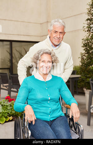 Senior come un visitatore nella clinica di riabilitazione spinge la donna come un paziente su una sedia a rotelle Foto Stock