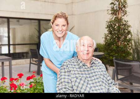 Cura geriatrica spinge infermiere uomo senior con corsa in carrozzella Foto Stock