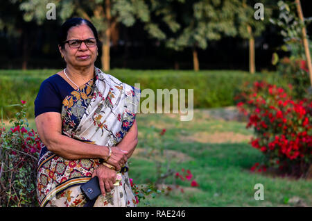 Ritratto di un senior donna indiana nel parco indiana che indossa gli abiti tradizionali (saree)con un background di bouganville in un parco a Delhi, India Foto Stock