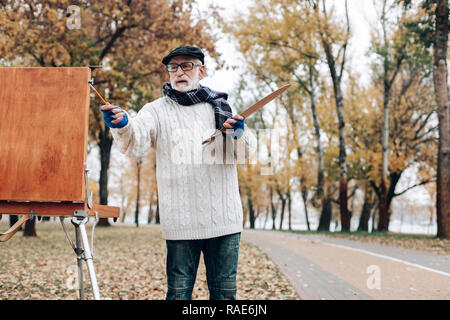 Attento pensionato in piedi vicino al suo cavalletto in legno Foto Stock