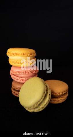 Amaretti francesi o macarons, la selezione di diversi colori e sapori, molto luminosa bite-size dolciumi, impilati ad alto isolato su sfondo nero Foto Stock