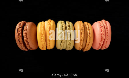 Amaretti francesi o macarons, la selezione di diversi colori e sapori, molto luminosa bite-size pasticceria, allineati e isolate su sfondo nero Foto Stock