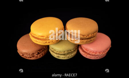 In stile tradizionale francese amaretti o macarons, la selezione di diversi colori e sapori, molto luminosa bite-size pasticceria, impilati e isolato su nero Foto Stock