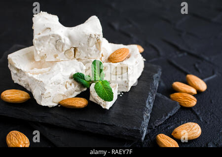 La deliziosa e tradizionale festa italiana torrone torrone o con i dadi sulla pietra nera dello sfondo. Torrone morbido blocchi con mandorle con foglie di menta fresca. H Foto Stock