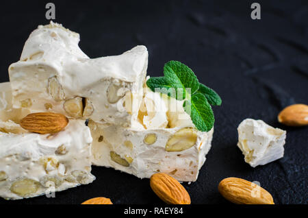 La deliziosa e tradizionale festa italiana torrone torrone o con i dadi sulla pietra nera dello sfondo. Torrone morbido blocchi con mandorle con foglie di menta fresca. H Foto Stock