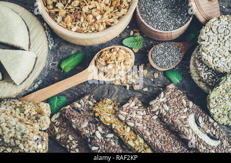 Spuntini salutari. Integratori alimentari. Halva di sesamo. Fiocchi, chia semi in due ciotole e cucchiai. Kozinaki, tre barrette energetiche e le foglie di menta. I grissini con fla Foto Stock