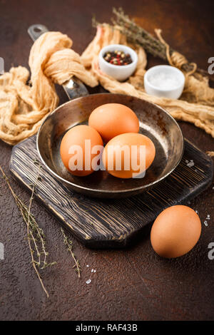 Pollo uova marrone e una padella piccola - un set per la realizzazione di uova strapazzate o una frittata, sale e spezie su uno sfondo marrone Foto Stock