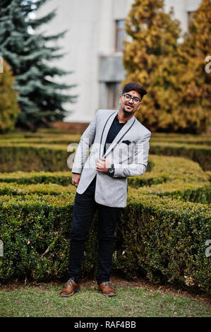 Elegante uomo indiano con bindi sulla fronte e bicchieri, usura sulla tuta poste all'aperto contro cespugli verdi al parco. Foto Stock