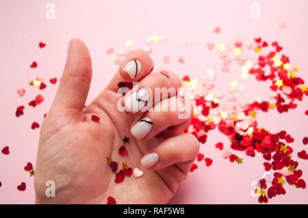 Giovane donna la mano con una bella manicure su sfondo rosa con il rosso a forma di cuore ad coriandoli. Foto Stock