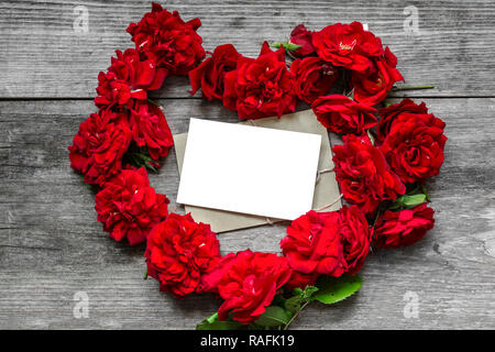 Forma di cuore red rose fiori con bigliettino vuoto sul legno rustico sfondo. Il giorno di San Valentino del concetto. vista dall'alto. mock up Foto Stock