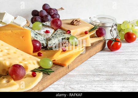 Vari tipi di formaggio servita sul tagliere di legno con uve, melograno, rosmarino e i pomodori ciliegia. close up Foto Stock