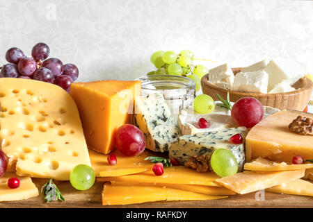 Vari tipi di formaggio con uve, rosmarino e melograno sul tagliere di legno. close up Foto Stock