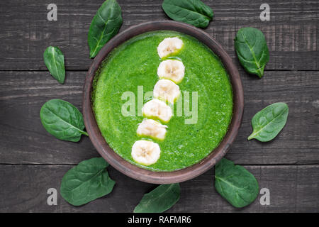 Verde sano frullato di spinaci ciotola e rabboccato con banana sul legno scuro sfondo, vista dall'alto. una sana prima colazione Foto Stock