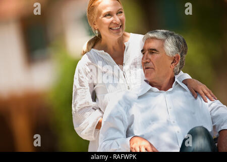 Senior uomo essendo spinto in sedia a rotelle dalla moglie. Foto Stock