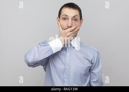 Sarò tranquilla. Scioccato bello imprenditore delle setole nella classica maglietta blu in piedi guardando la telecamera con occhi grandi e che copre la sua bocca. interna st Foto Stock