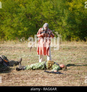 Festival storici Sambek altezze. Mujahid sul campo di battaglia tra i morti soldati sovietici Foto Stock