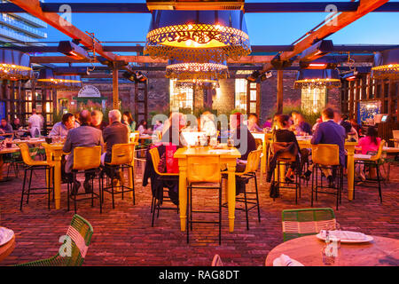 Le persone hanno la cena presso il patio di un ristorante nel quartiere di distilleria di Toronto, Canada come visto dal marciapiede. Foto Stock