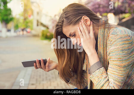 Vista laterale della giovane donna tenendo il telefono e cercando felice con rottura mentre è seduto sulla strada Foto Stock