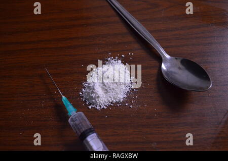 Narcotici essendo preparato. Aghi, cucchiaio e polvere bianca su una tabella. Foto Stock