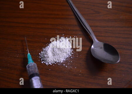 Narcotici essendo preparato. Aghi, cucchiaio e polvere bianca su una tabella. Foto Stock