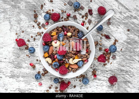 Cioccolato artigianale muesli muesli o in una ciotola con un cucchiaio, bacche, frutta secca e noci. Colazione sana. vista superiore Foto Stock