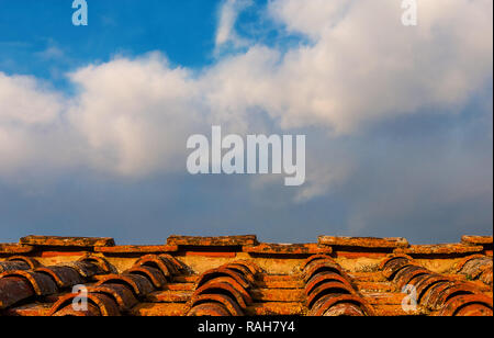 Vecchie piastrelle in ceramica con tetto di licheni, nuvole e cielo blu sopra come sfondo (con copia spazio) Foto Stock