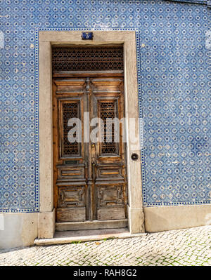 Lisbona - Portogallo, facciata di una casa coperta con tipiche piastrelle blu, azulejos e la vecchia porta di legno con decorazioni in metallo Foto Stock
