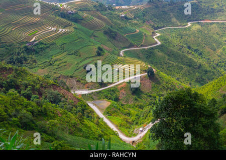 Avvolgimento di stretta strada che conduce ad un piccolo villaggio di montagna circondato da polpette di riso e campi di mais. Ha Giang Loop, Ha Giang Provincia, Vietnam Asia Foto Stock