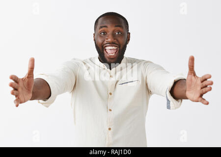 Vieni tra le mie braccia. Ritratto di gioiosa cordiale e felice bello African American uomo con barba e capelli corti, sorridente largamente e tirando le mani verso la telecamera per esprimere un caloroso abbraccio o coccola Foto Stock