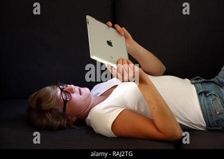 Giovane donna sdraiata su un divano e il surf con un iPad, tablet PC, accesso wireless a internet Foto Stock